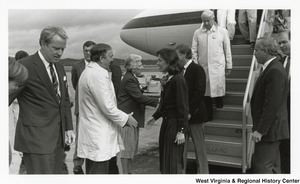 Governor Arch Moore disembarking from an airplane. At the bottom of the stairs stands his wife, Shelley, who with an unidentified man, is greeting the other passengers.