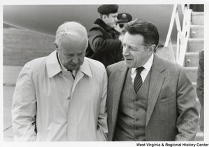 Governor Arch Moore speaking with an unidentified man. Behind them is an airplane and two unidentified men.
