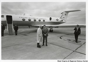 Governor Arch Moore speaking to an unidentified man on a tarmac. An airplane is behind them with the door open.