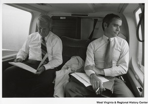 Governor Arch Moore riding in a vehicle with an unidentified man. Governor Moore is looking at a document and the other man is looking out the window.
