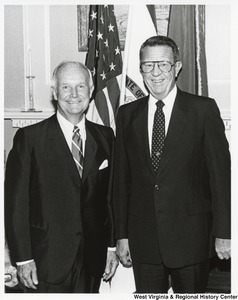 Governor Arch Moore standing with an unidentified man in front of the American flag and West Virginia flag.