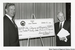 Governor Arch Moore (right) and an unidentified man standing beside a giant check that awards the citizens of Bluefield $175, 287 dollars.