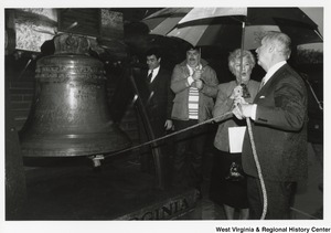 Governor Arch Moore ringing the Liberty Bell replica at the State Capitol. Shelly Mooe and two unidentified men are with Governor Moore as he rings the bell. The bells inscription reads: Proclaim liberty throughout all the land unto all the inhabitants therof Lev XXVX. By order of the assembly of the province of Pennsylvania for the state house in Philada. Pass and Stow. Philada. MDCCLIII.