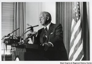 Governor Arch Moore speaking at a press conference. The Governor is leaning against the podium and pointing at the crowd.