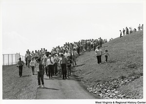 Governor Arch Moore (center of trail in white shift with tie) leading a large group of people down a hill.
