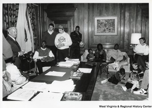 Governor Arch Moore (standing first on the left) talking with a group of men, women, and kids in his office.