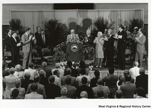 An unidentified man is being given a standing ovation after a speech. Standing to the right of the speaker is: Governor Arch Moore, an unidentified woman, Senator Robert C. Byrd, and Senator Jay Rockefeller.