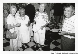 Three unidentified woman and one man smile at the camera. They appear to be at a party.