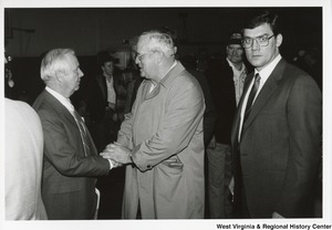 Governor Arch Moore shaking the hand of an unidentified man. Another unidentified man (right corner) is looking at the camera.