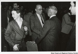 Governor Arch Moore standing with his back to camera and shaking the hand of an unidentified man. An unidentified boy is beside them looking behind himself.