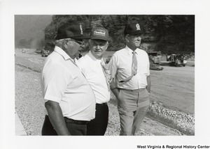 Governor Arch Moore standing outside with two unidentified men. Governor Moore is wearing a hat that reads Explosive Demtech Demolition.