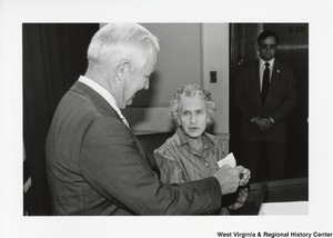 Governor Arch Moore with an unidentified woman. Governor Moore is looking at a small piece of paper and smiling.