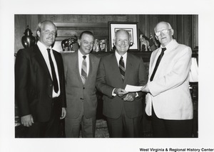 Governor Arch Moore (second from right) standing in front of a mantle with three unidentified men. Governor Moore is taking a slip of paper from one of the men.