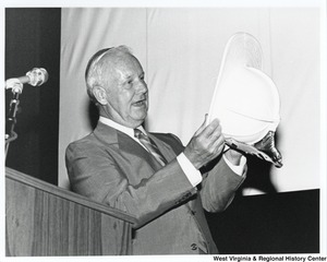 Governor Arch Moore standing at a podium looking at the inside of a hardhat.