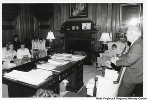 Governor Arch Moore standing behind his desk chair talking to a group of kids and teens situated around his office.