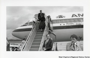 An unidentified woman is disembarking from a plane. Walking right behind her is an unidentified man, Governor Arch Moore, and another unidentified man.
