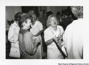 Two unidentified women laughing during a party. Three other unidentified women are around them.