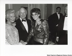 An unidentified woman is shaking Shelly Moores hand during a party. Governor Arch Moore is standing between them. They are all looking at the camera.
