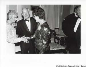 An unidentified woman is shaking Shelly Moores hand during a party. Governor Arch Moore is standing between them.
