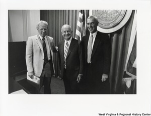 Governor Arch Moore standing with two unidentified men before the Great Seal of West Virginia.
