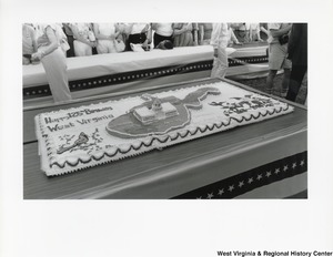 A large sheet cake celebrating the 125th birthday of the state. The cake features the state of West Virginia in the center with the capitol building in the center of the state. On the left corner of the cake is a cardinal and above it is the words Happy 125th Birthday West Virginia. On the right corner is rhododendrons with 1863-1988 below it.