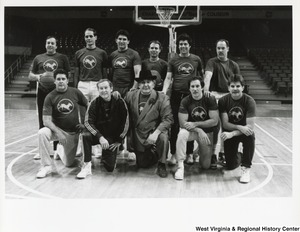A basketball team on a basketball court. The team members are wearing t-shirts with a running dog in a circle. The front row is down on one knee while the second row is standing.