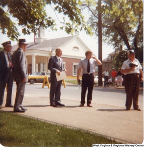 Governor Arch Moore (third from the left) standing outside on a sidewalk with five unidentified men on Memorial Day.