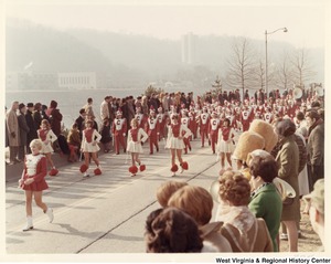 A high school marching band during Governor Arch Moores inaugural parade in Charleston. The band is wearing red and white marching band uniforms with a red C on them.