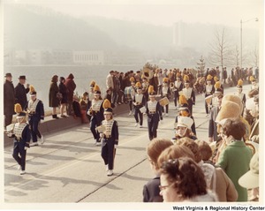 A high school marching band during Governor Arch Moores inaugural parade in Charleston. The band is wearing dark blue and white marching band uniforms with gold accents.