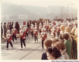 A high school marching band during Governor Arch Moores inaugural parade in Charleston. The band is wearing red and white marching band jackets with black pants. The jackets have a red S on them.