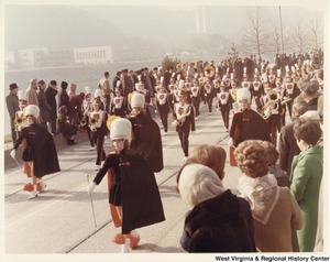 An unidentified high school marching band during Governor Arch Moores inaugural parade in Charleston. The band is wearing black uniforms with white and red accents. In the center of the jacket is a bear.