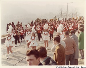 An unidentified high school during Governor Arch Moores inaugural parade in Charleston. The band is wearing red and black uniforms. The majorettes are wearing white uniforms with red accents.